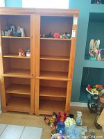Front view of the solid wood bookcase showing two side-by-side sections, each with five shelves, with various decorative items on some shelves. Light wood finish and traditional style base molding visible.