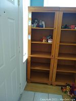 Solid wood bookcase positioned next to a door, showing full height and five shelves, empty except some decorative items on upper shelves.