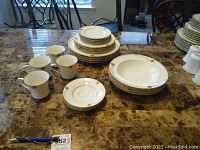 Full set of dinnerware on marble table including cups, plates in various sizes, bowls and saucers arranged and shown clearly