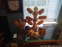 Photo of carved wooden cups on stands, ceramic piggy bank, animal figurines and dried floral decor displayed on a glass table near window.