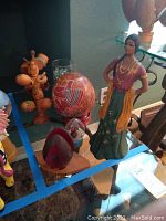 Wide view showing four small wooden cups on a tiered stand, ceramic female figurine in traditional clothing, painted gourd, and other decorative items.