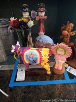 Photo showing the glass flowers in a vase, the ceramic hand painted cow bank, the sunflower face figurine, a painted egg decor piece, and two nutcracker figurines.