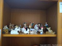 Shelf with multiple miniature porcelain and ceramic figurines including birds, angels, clowns, and other characters.