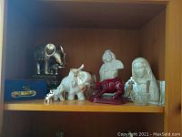 Shelf shows multiple white elephant figurines, a red bull figurine, two white bust sculptures, and a crystal piece with Christ image.