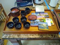 Full lot displayed on teak tray showing all items: black ceramic bowls and mugs, decorative pottery, wooden plate, colorful Australian cityscape coasters, and box of geode coasters.