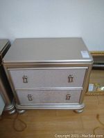 Front angled view of silver night stand showing two drawers with metal handles, silver finish, and visible surface wear marks on top.