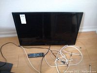 Full view of Element LCD television on floor with remote and cables.
