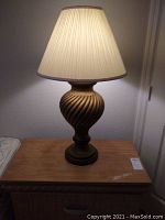 Table lamp lit showing pleated shade and spiral swirl base details on wooden furniture.