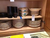 Mikasa Garden Club Bells of Blue dinnerware sets arranged on a wooden shelf showing stacks of plates, bowls, cups, and saucers.