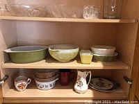 Glassware and Pyrex bowls on shelves in wooden cabinet.