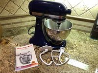 KitchenAid KSM90BU stand mixer in royal blue with stainless steel bowl, dough hook, flat beater, and manual on granite countertop.