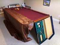 Full view of American Heritage pool table with burgundy felt and draped vinyl cover