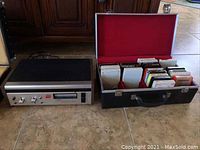 Full view of the Concord 8-track tape recorder/player beside its carrying case filled with 19 8-track tapes