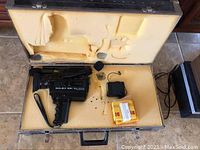 Top-down photo showing the Bolex 551 XL Sound Macrozoom Super 8 camera inside its molded hard carrying case along with power adapter and a yellow package of new film tape.