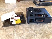 Photo of the Kodak Extra Sound Movedeck projector with manuals and a practice sound film on the floor.