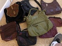 Full assortment of over ten ladies purses arranged on the floor showing variation in color and style.