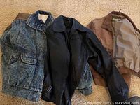 Three men's jackets laid out showing two black leather jackets and one denim jacket, all worn.
