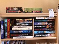 Books stacked on wooden shelves with visible titles including Bourne Ultimatum, The Hobbit, Neon Rain, Outfox