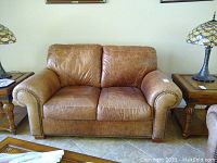 Front view of brown leather loveseat showing two seat cushions and rolled armrests with nailhead trim.