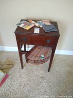 Full view of antique wooden sewing cabinet with drawer and semi-circular drop-down compartment, showing some sewing essentials arranged on top.