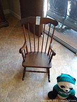Full view of child's wooden rocker with high back and armrests, showing general condition and included stuffed panda toy.