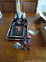 Photo of lacquered trays, wood carved birds, African figurines, small pyramid model, and painted vase on wooden table