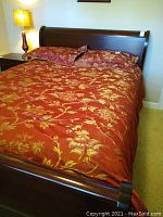 Full bed shown made with queen red and gold quilt and two matching pillow shams in a bedroom setting.