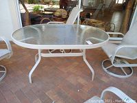 Full view of glass topped patio table showing glass and white metal frame with 4 legs and base supports.