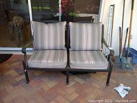Front view of metal patio bench with two striped cushions and black metal frame.
