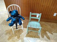 Photo showing antique green child chair with distressed paint and white child chair with blue teddy bear seated on it