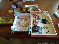 Overview of multiple jewelry items, necklaces, earrings, charm, and watch parts on table.