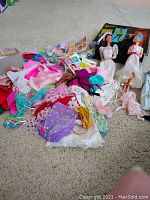 Photo showing two Barbie or Barbie-type dolls next to a large pile of assorted Barbie clothing and accessories.