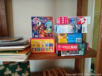 Shelf photo showing the stacked boxed puzzles and Disney-themed tray puzzles and books.
