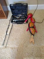 Photograph showing clarinet in open blue case, metal flute, and three wooden maracas on carpeted floor.