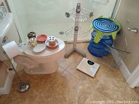 Photo showing collection of bathroom items: toilet paper holder, scale, shower organizers, mesh hamper, and ceramic bathroom accessory items.