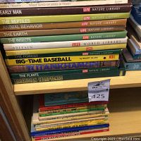 Stack of Life Nature Library books and sports books on a wooden shelf.