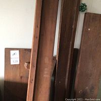 Photo showing three long wooden shelving boards with metal brackets and one shorter board leaning against a wall.