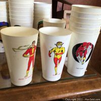 Photo of collectible cups featuring superheroes Shazam, The Flash in red and yellow costumes.