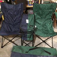 View of both sides of the collapsible chair, green side with a visible small tear and navy blue side, alongside the green carrying case.