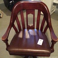 Front view of wooden banker's chair with brown leather seat and curved slatted backrest.