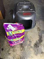 Photo of gray Natures Miracle covered cat litter box with front entry and ventilation at top, accompanied by a purple bag of Scoop Away Complete Low Dust cat litter.