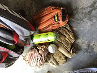 Photo of baseball gloves, baseball, and tennis ball tube on concrete floor