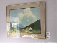 Front view of framed landscape artwork showing mountains, water, cottage, beige linen matting, and gold frame.