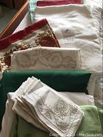 Photo showing a stack of various table linens and napkins in white, red, and green colors with embroidery and woven designs.