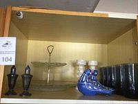 Photo of assembled items on shelf including sterling silver shakers, blue ceramic birds, candleholders, glasses, and two-tier platter.