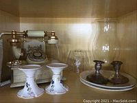 Shelf display showing Royal Terra floral candleholders, sterling silver candleholders, vintage phone, clear glass vase, and china plates.