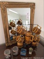 Mid century ceramic coffee set arranged on black metal rack in front of gold framed wall mirror, showing six mugs, coffee pot, creamer, and sugar bowl