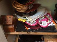 View of assorted baskets, cutting boards, wooden knife block, fabric pot holders, and silver plated tray stacked on a shelf.