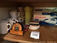 Photo of white coffee mugs, yellow Pyrex pitcher, Ecuador coasters, and boxed Sunbeam electric knife.