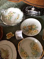 Photo showing vintage Czech china plates with yellow floral designs, a silver-tone metal butter dish, ceramic flower figurine, and green pot.